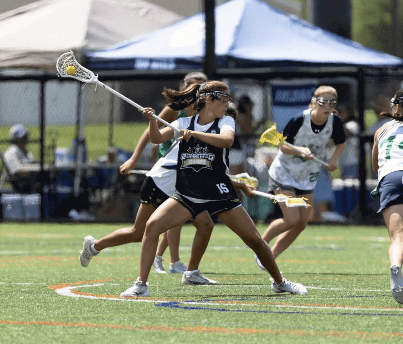 Girls playing lacrosse on a sunny field.