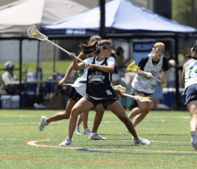 Girls playing lacrosse on a sunny field..
