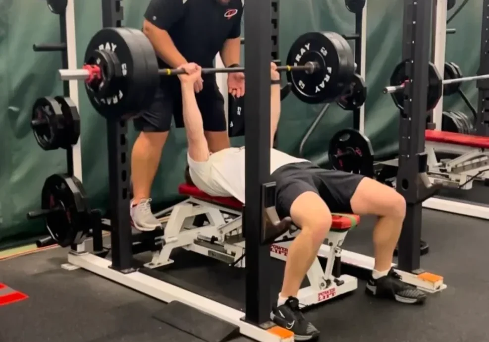 Person bench pressing with a spotter assisting.